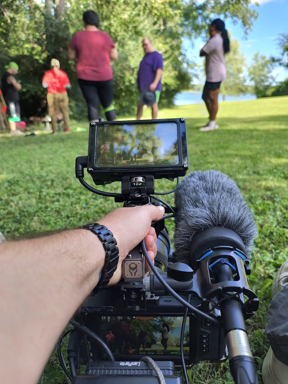 Point of view over a rigged cinema camera and monitor filming an outdoor group session by a lake