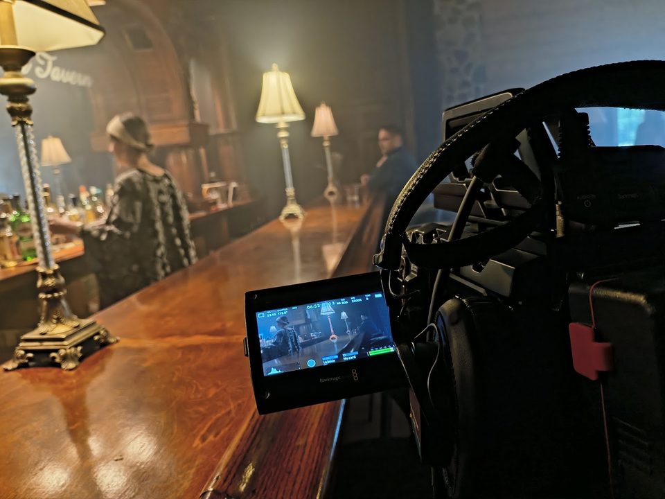 Behind the scenes on a narrative shoot in a candlelit tavern, cinema camera and monitor in the foreground